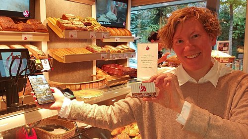 Friederike Tebbe, Geschäftsführerin der Konditorei und Bäckerei Welpinghus, präsentiert zwei der drei Möglichkeiten zum bargeldlosen Bezahlen: die geschäftseigene App und die Vorteilskarte. - © Claus Meyer
