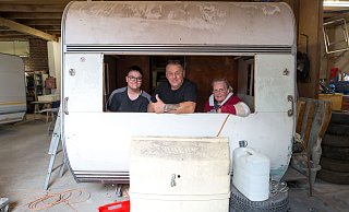 Justin (v. l.), Uwe und Anke Gruhle schauen aus dem Fenster eines Wohnwagens. Bis in das Urlaubsgefährt wieder Leben einkehrt, wird es in der Versmolder Werkstatt aber noch dauern. - Andre Schneider