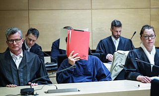 Prozess im Mai 2023: Einer der Angeklagten versteckt sein Gesicht hinter einem roten Aktendeckel. Er wird von den Strafverteidigern Detlev Binder (l.) und Susanne Renner vertreten. Hinter ihnen sitzt der zweite Angeklagte, der ebenfalls unerkannt bleiben will. - Sarah Jonek
