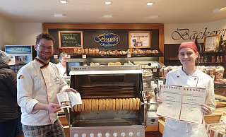 Geschäftsführer Patrik Kröger mit dem "Feinschmecker" und Mitarbeiterin Jana Kolbe mit den Urkunden der Produktprüfungen präsentieren die Spezialität des Hauses: Den Baumkuchen. - Tobias Barrelmeyer