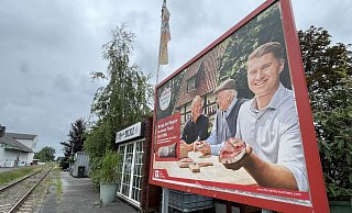 Auf den aktuellen Werbeplakaten sitzen drei Generationen der Familie Reinert am Esstisch. Carl Reinert (r.) nimmt eine auffallend präsente Position ein, während im Hintergrund Vater Hans-Ewald und Großvater Hans ins Gespräch vertieft scheinen. - Tasja Klusmeyer