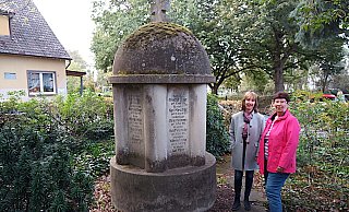 Anja Pohlmann (links) und Karin Kozlowski von der UWG-Fraktion stehen neben dem alten Schulgebäude am Ehrenmal, das an die Gefallenen des ersten Weltkrieges erinnert. Das Ehrenmal soll nach ihrem Vorschlag versetzt werden. - Ekkehard Hufendiek
