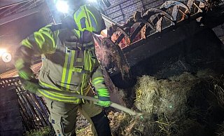 Ein Feuerwehrmann zieht Stroh auseinander, um nach versteckten Glutnestern zu suchen. - Feuerwehr Borgholzhausen