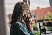 Eine Frau telefoniert am Fenster - Zacharie Scheurer/dpa-tmn