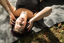 Eine diverse Person mit Kopfhörern im Park - Christin Klose/dpa-tmn