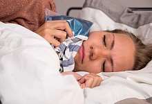 Eine Frau hält sich im Bett einen Kühlakku an die Wange - Christin Klose/dpa Themendienst/dpa-tmn