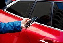 Eine Person steht mit einem Smartphone neben einem Auto - Bernd Diekjobst/dpa-tmn