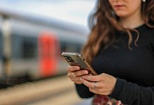 Eine junge Frau steht mit ihrem Mobiltelefon auf einem Bahnsteig - Jan Woitas/dpa/dpa-tmn