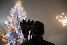 Ein Mann mit Feuerwerksraketen vor einem Weihnachtsbaum - Lino Mirgeler/dpa-tmn