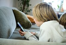 Junge liegt auf einem Sofa und guckt auf sein Smartphone - Annette Riedl/dpa/dpa-tmn