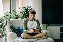 Ein junger Mann sitzt mit Smartphone auf einem Sessel - Zacharie Scheurer/dpa-tmn Ein junger Mann sitzt mit Smartphone auf einem Sessel - Zacharie Scheurer/dpa-tmn