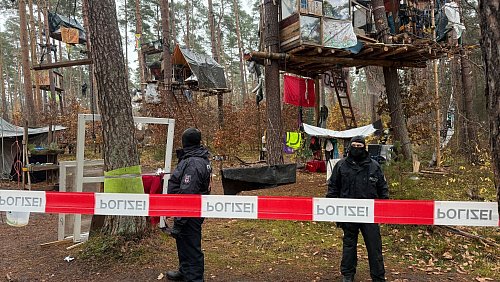 Polizeikräfte sichern das Waldgebiet hinter einer Absperrung. Umweltaktivisten, die gegen Tesla protestieren, müssen ihr Camp räumen. - © Lutz Deckwerth/dpa