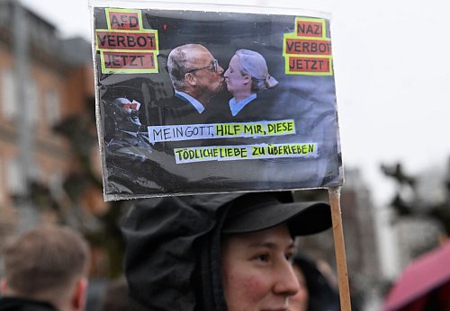 Drastische Kritik bei der Demonstration: Auf einer Fotomontage küssen sich Merz und Weidel. - © Roberto Pfeil/dpa