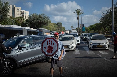 Ein israelischer Demonstrant geht mit einem Schild auf einer Straße, während Autos sich stauen. - © ILIA YEFIMOVICH/dpa