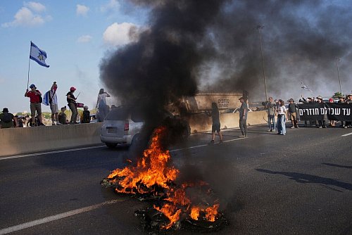 Israelische Demonstranten blockieren eine Straße bei einem Protest. - © Ohad Zwigenberg/AP/dpa