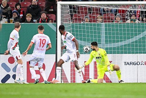 Der Schuss, der zum Augsburger Pokal-K.o. führt. Verteidiger Chrislain Matsima (M) fälscht den Ball auch noch unglücklich und damit unhaltbar ab. - © Harry Langer/dpa