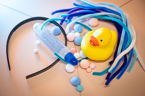 Material für den Enten-Kopfschmuck: ein Quietsche-Entchen, ein Haarreif, viele Pfeifenreiniger und Bommeln sowie Kleber. - © Christin Klose/dpa-tmn