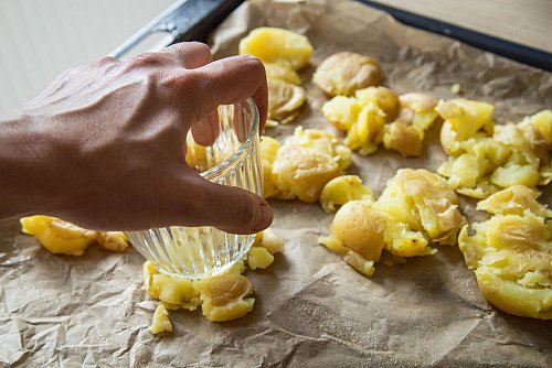 Die gekochten Kartoffeln kommen auf ein Backblech und werden mit einem Glas zerdrückt. Mit Olivenöl bepinseln und Salzflocken bestreuen, dann 40 bis 45 Minuten knusprig backen. - © Christin Klose/dpa-tmn