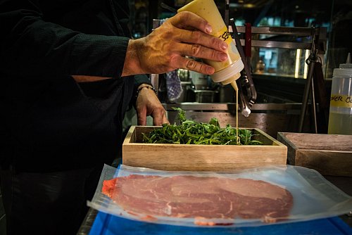 René Tepper träufelt im «The Dry Gin and Beef Club» für ein Carpaccio eine Vinaigrette auf die Rucolablätter. - © Christin Klose/dpa-tmn