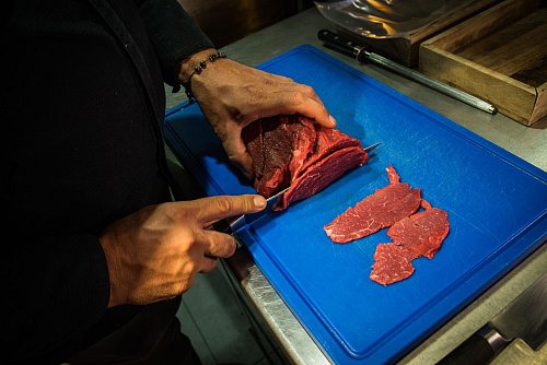 Mit einem scharfen Messer schneidet René Tepper dünne gleichmäßige Scheiben vom Rinderfilet ab. - © Christin Klose/dpa-tmn