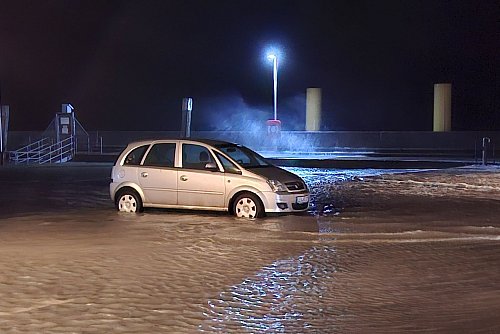 In Wilhelmshaven steht ein Auto auf einem überfluteten Parkplatz. - © Kai Moorschlatt/dpa