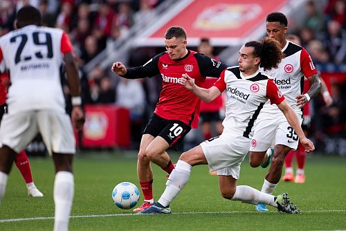 Für den Ex-Leverkusener Florian Wirtz (M) kommt es am Mittwoch zum Wiedersehen mit Eintracht Frankfurt um Arthur Theate (r). (Archivbild) - © Marius Becker/dpa
