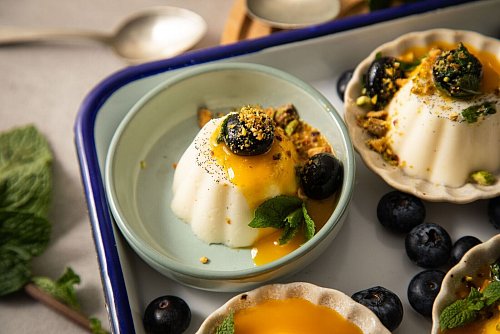 Deko-Vorschlag für die Vanille-Panna Cotta: mit Mangosoße, Blaubeeren, Minze und Pistazien verzieren. - © Christin Klose/dpa-tmn