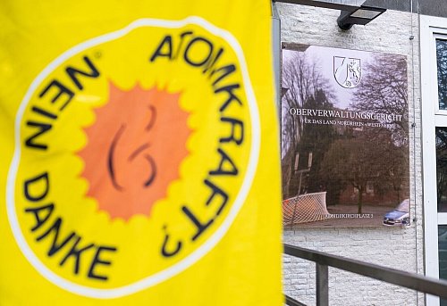 Vor der mündlichen Verhandlung im Streit um die Lagerung des Jülicher Atommülls im Zwischenlager Ahaus steht eine Demonstrantin mit einer «Atomkraft? - Nein Danke»-Fahne vor dem Oberverwaltungsgericht (OVG). - © Guido Kirchner/dpa
