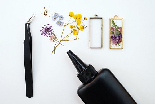 Eine Pinzette, getrocknete Blüten, einen fertigen Anhänger und UV-Harz - dieses Material braucht es zum Basteln des Anhängers. Handschuhe und UV-Schutzbrille nicht vergessen. - © Franziska Gabbert/dpa-tmn