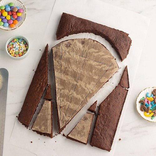 Ein klassischer Schokokuchen auf einem Blech mit Backrahmen ist die Basis für den Schultütenkuchen. Die zuvor gezeichneten Vorlagen auf Backpapier werden dann darauf gelegt und an den Rändern entlang zugeschnitten. Mutige können natürlich auch ohne Vorlage frei Hand zuschneiden. - © Kathrin Runge/backenmachtgluecklich.de/dpa-tmn