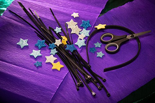 Material für den Sternen-Kopfschmuck: schwarze Kabelbinder, ein Haarreif, selbstklebende Glitzersterne aus Moosgummi und eine Schere. - © Christin Klose/dpa-tmn