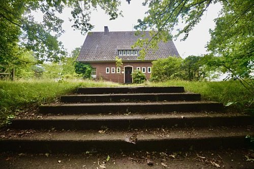Sechs breite Stufen führen auf den kurzen Weg zur Eingangstür der alten Kommandanten-Villa auf dem ehemaligen Flughafen in Gütersloh. Rundherum ist alles verwildert. - © HK